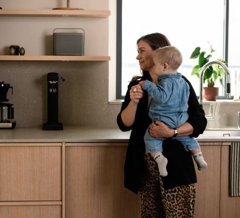 Eine Frau mit Baby im Arm steht in der Küche und schaut auf den Absodry Raumentfeuchter hinter ihr im Regal