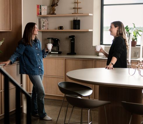 Preview: Zwei Frauen unterhalten sich in einer Küche. Im Hintergrund steht dezent und unauffällig ein schwarzer Absodry Raumentfeuchter im Regal.