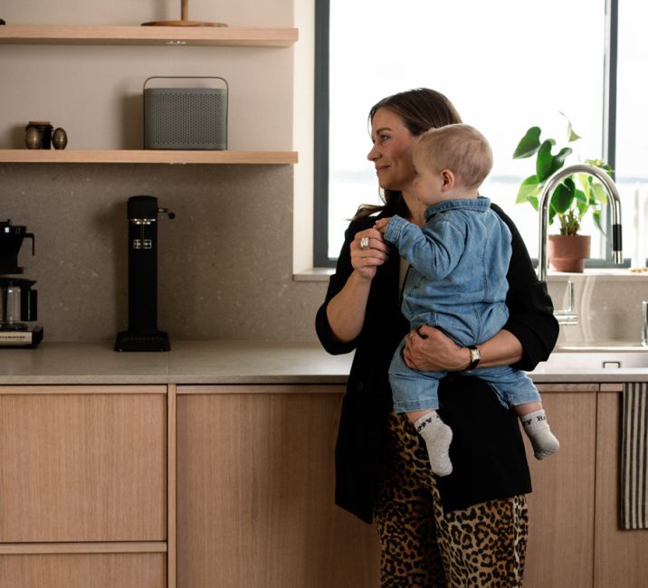 Eine Frau mit Baby im Arm steht in der Küche und schaut auf den Absodry Raumentfeuchter hinter ihr im Regal